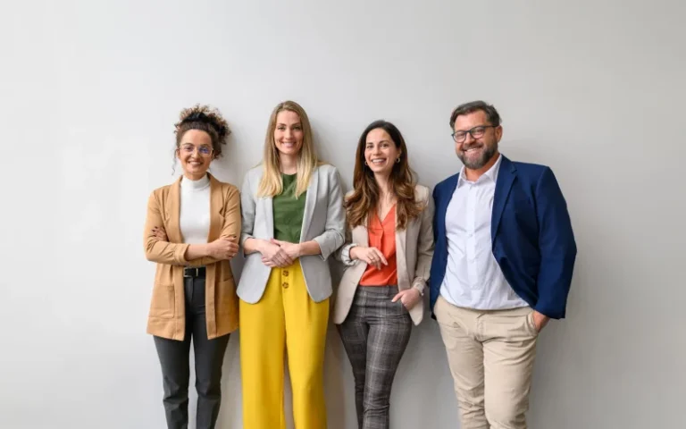 Four smiling professionals standing side-by-side against a plain white wall